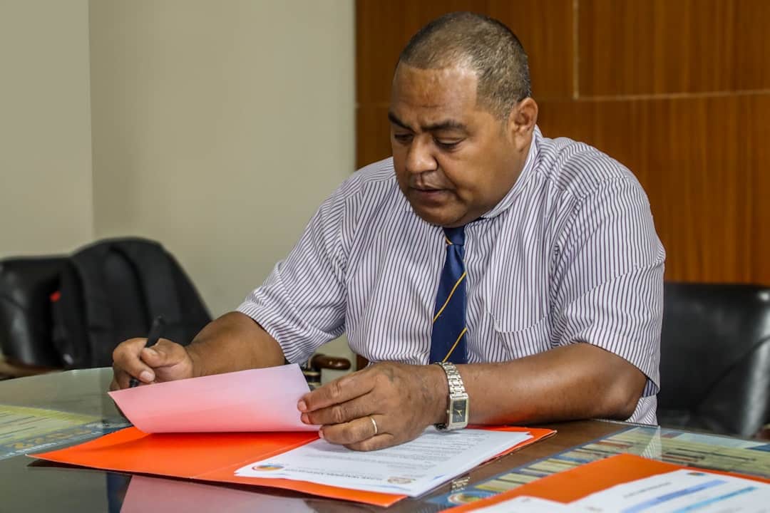 A close-up shot of a man's hands as he carefully reviews a contract at a clean, modern table, holding a pen and appearing focused and confident.