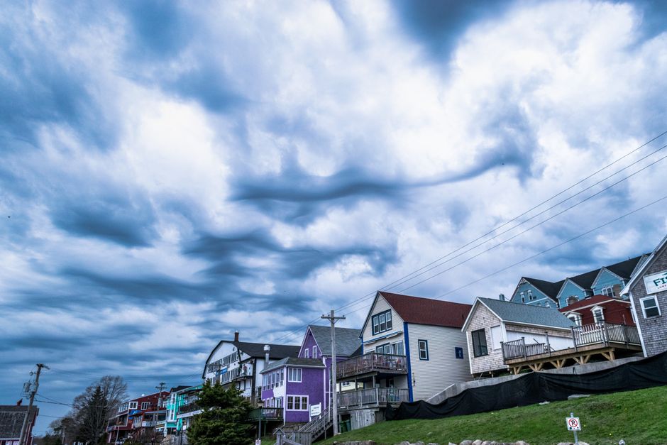 A dramatic image of dark, turbulent storm clouds gathering above a sturdy suburban home, symbolizing the threat of severe weather to a residential property.