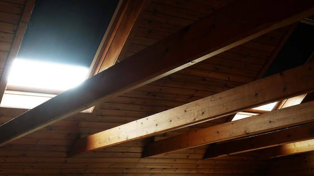 A home inspector or contractor shines a flashlight into a dark attic to assess the condition of the existing insulation and structure.