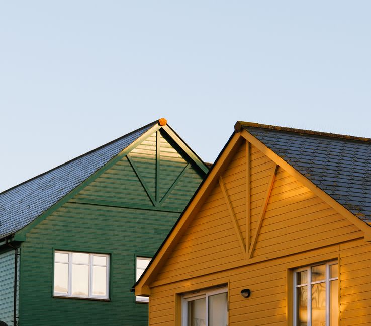 A person standing in their yard looking up thoughtfully at the roof of their home, considering its condition and safety.