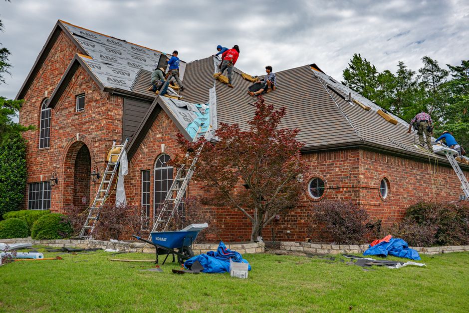 A skilled roofer in safety gear meticulously installing new asphalt shingles on a residential rooftop under bright sunlight.